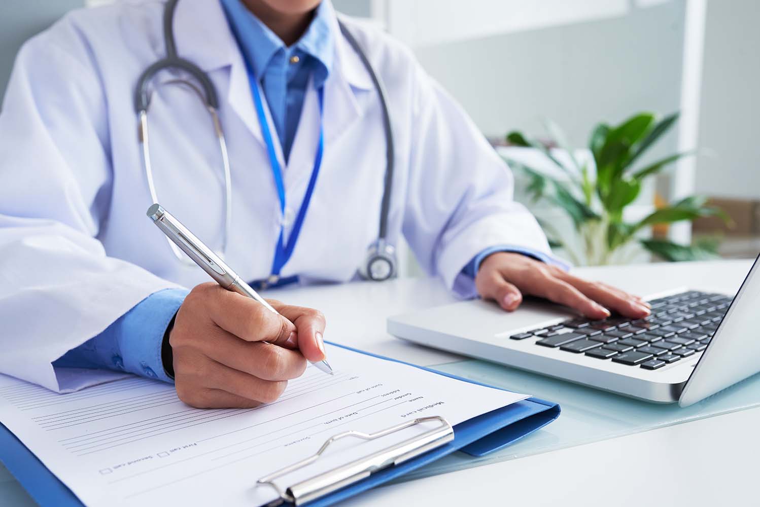 hands-unrecognizable-female-doctor-writing-form-typing-laptop-keyboard